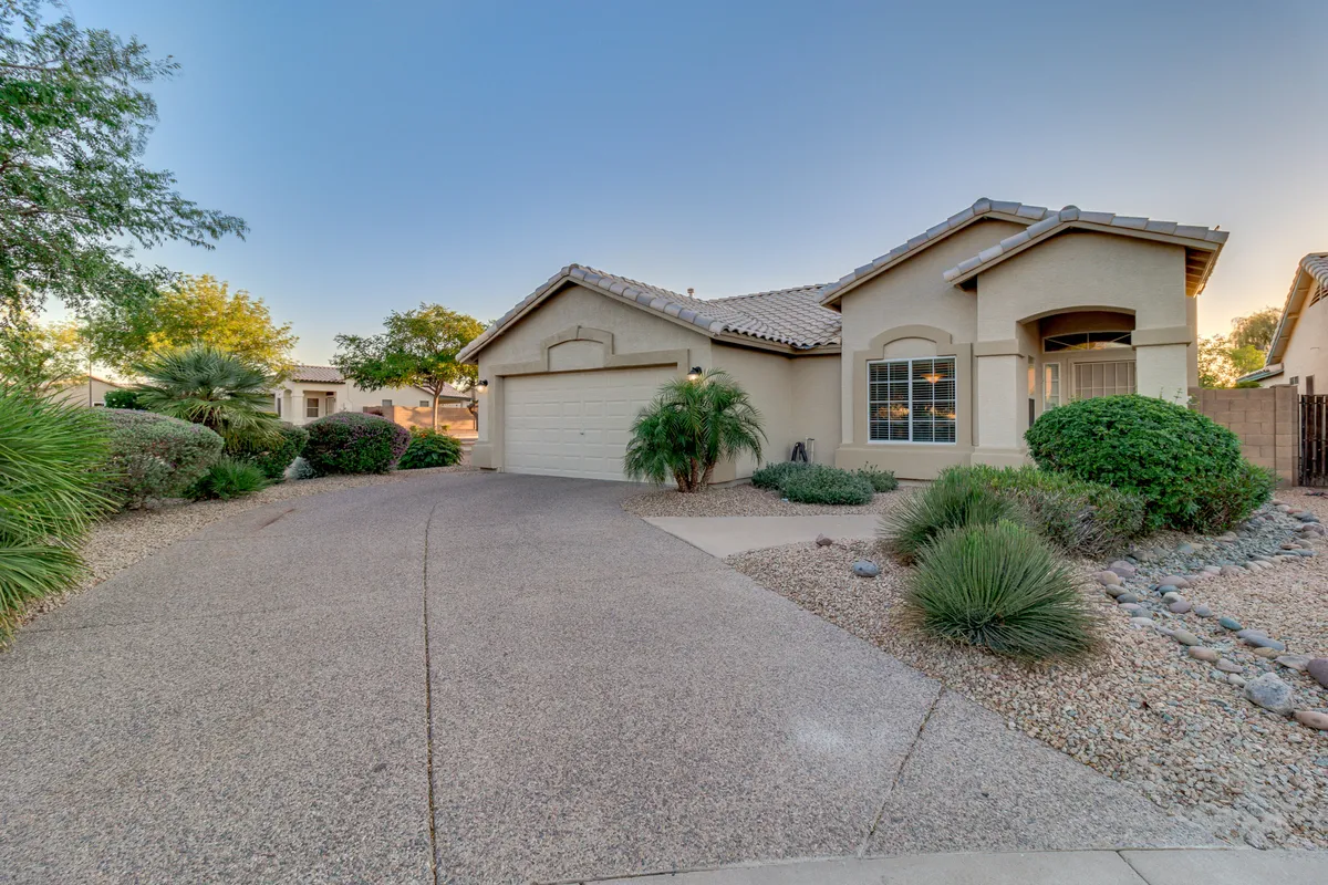 The image highlights the front door and garage set within a beautifully landscaped garden, under soft natural light. Family members can be imagined gathering, relaxing outdoors, or preparing for an evening stroll.