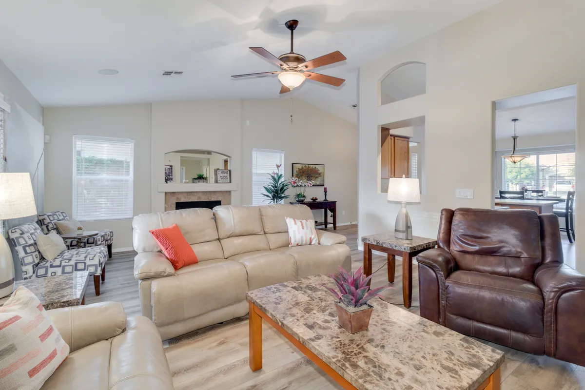 Showcasing a spacious open-plan living room, the image captures comfortable seating grouped around a chic coffee table with a decorative plant. The layout is open and airy, with elegant light fixtures and a backdrop of updated flooring and subtle artwork, making it ideal for social gatherings and relaxed conversations.