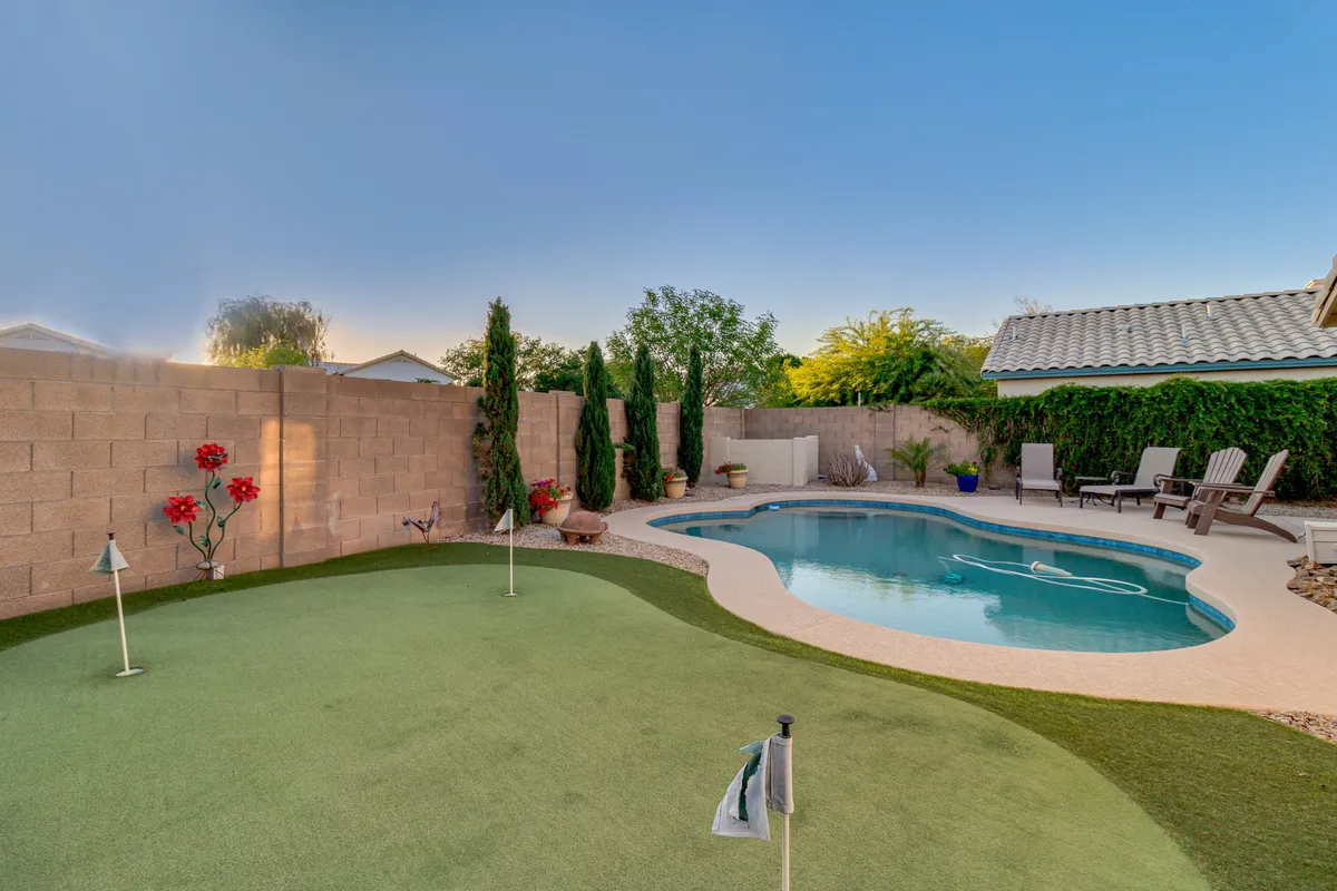 This image captures a beautifully landscaped backyard featuring a sparkling swimming pool, a private putting green, and ample outdoor seating. The lush greenery and manicured lawn create a luxurious and inviting atmosphere, perfect for relaxation or entertaining guests.