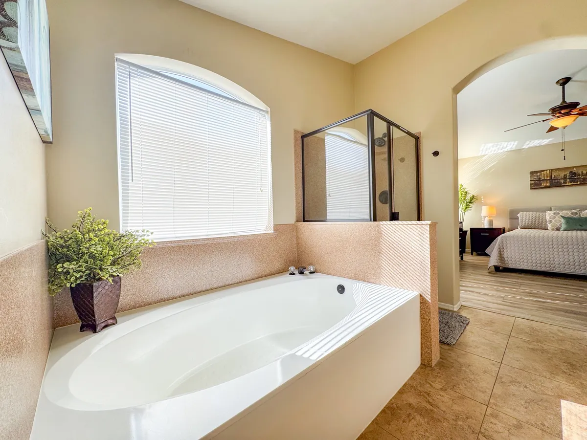 A spa-inspired bathroom with a modern soaking tub, glass-enclosed walk-in shower, and a large window letting in ample daylight. A decorative plant adds a touch of tranquility, and the overall aesthetic is inviting and luxurious.