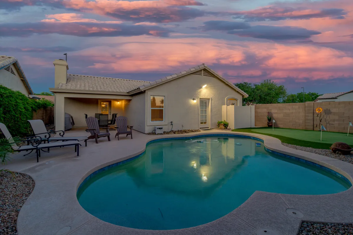 This exterior shot showcases the sparkling swimming pool, inviting patio seating, and the house's exterior set against a colorful Arizona sky. The scene blends the excitement of refreshing swims and relaxed gatherings, with the sunset hinting at memorable evenings spent outdoors.
