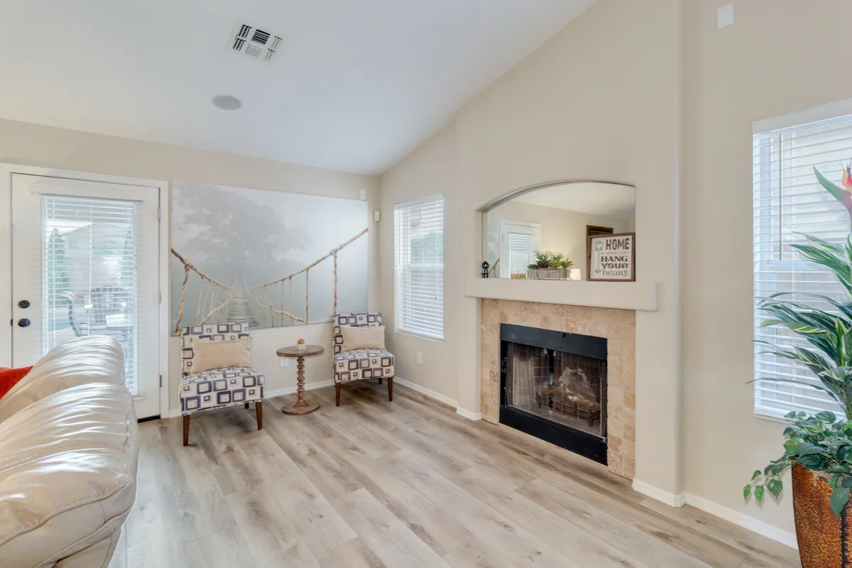 A cozy sitting area is centered on a fireplace, surrounded by plush seating and accentuated by a dramatic bridge mural and lush indoor plants. Ample natural light streams in, highlighting the inviting warmth and sophisticated touches that set the tone for memorable gatherings.
