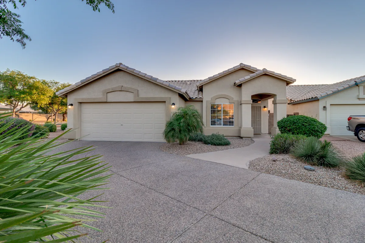 A welcoming view of the home's front entrance, landscaped yard, and garage door. The scene evokes the sense of coming home, with space for children to play and neighbors to gather. The landscaping and porch area connect the home to its friendly neighborhood context.