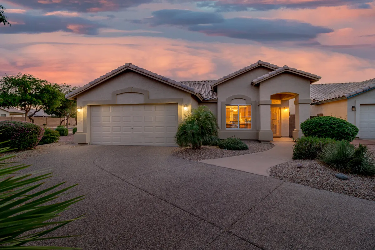 This exterior view presents the front door, garage, and lush landscaping, with space for gathering and relaxing. The warm, welcoming ambiance hints at a lifestyle filled with community connection and outdoor enjoyment.