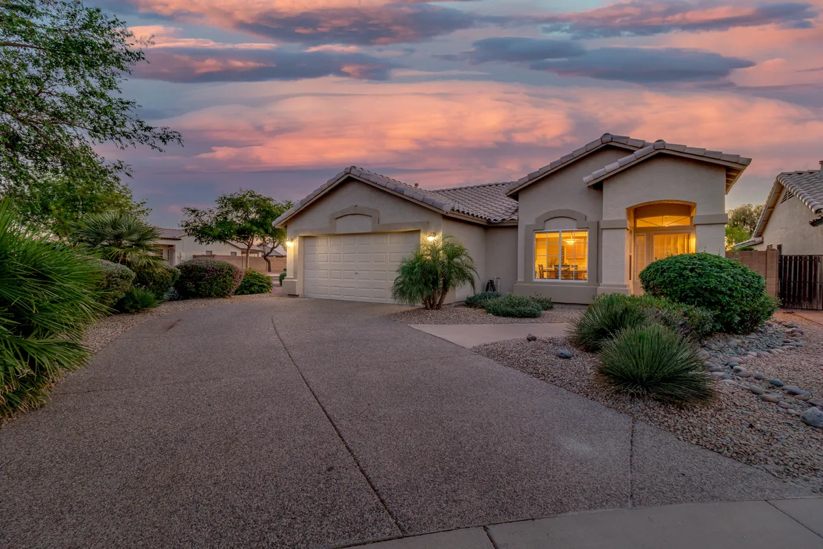 This exterior shot captures the welcoming facade of the home, featuring the driveway, landscaped front yard, and a picturesque sunset sky. The scene conveys the experience of stepping out into the neighborhood, ready to embark on a walkable adventure.