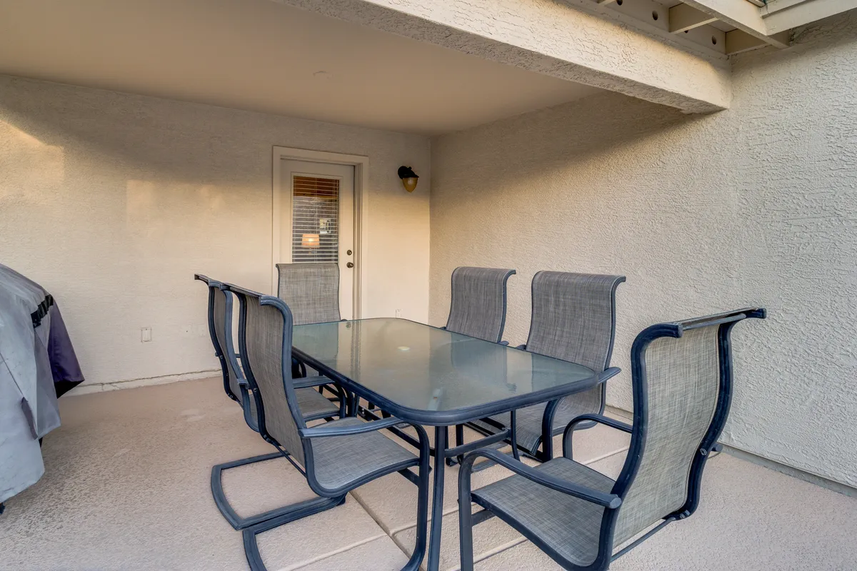 A stylish outdoor dining area set with a glass table and modern chairs, situated adjacent to the home’s entry. The patio is designed for alfresco meals and social gatherings, with a welcoming ambiance that invites relaxation and connection.